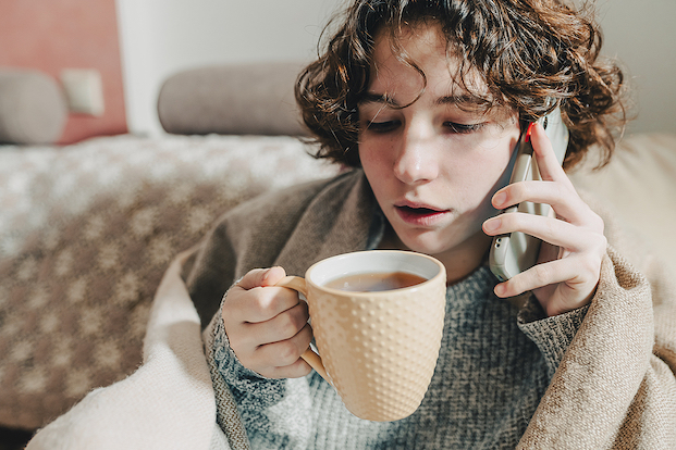 Woman sitting on chair, keeping warm with blanket over shoulders and hot chocolate.